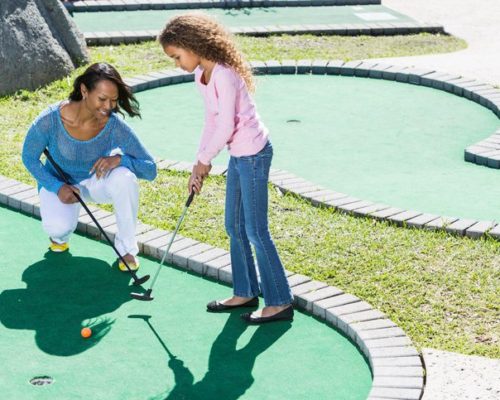 African American mother (30s) and daughter (9 years) playing miniature golf.