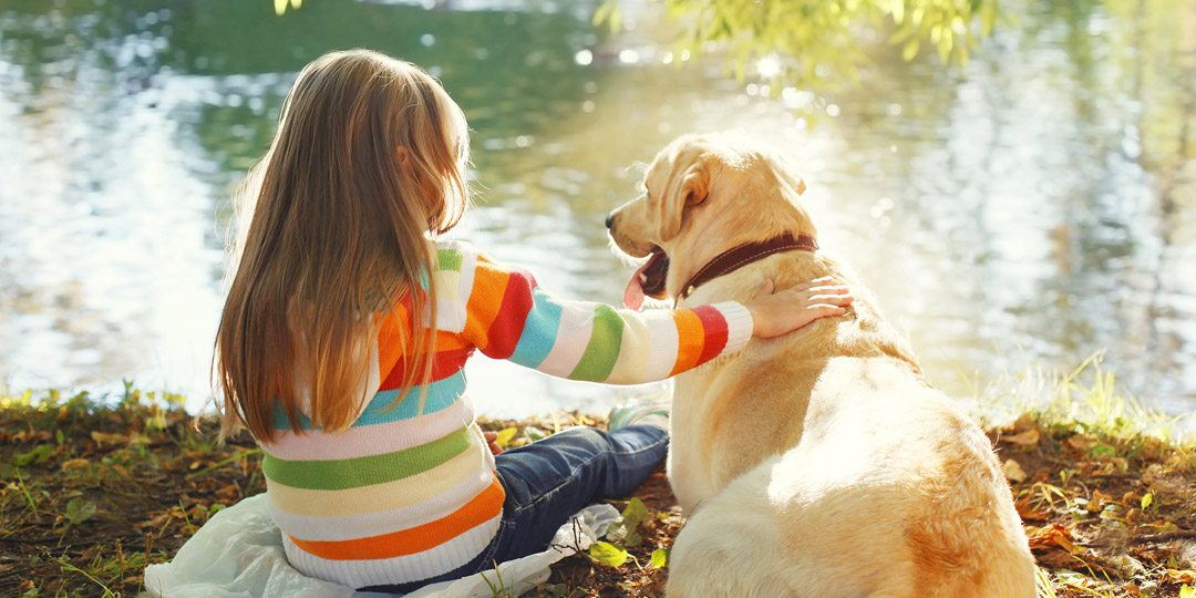 Little girl sitting with dog at lake