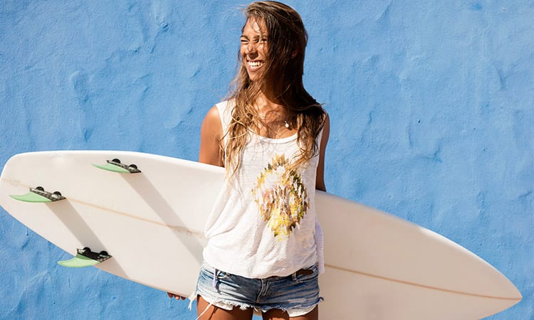 Surfer woman holding surfboard in front of blue wall